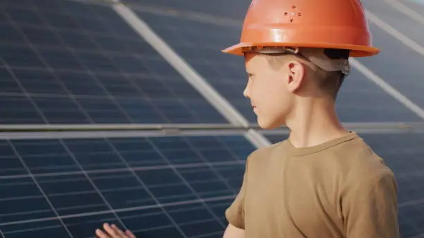 Photo of Little boy in a protective helmet at a solar power plant. The concept of children and green energetics. Children for clean energy. Shooting at a solar power plant. Ecological farm. Solar power station