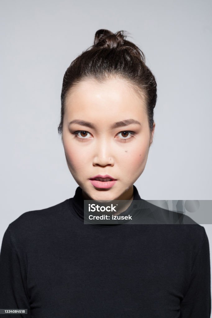 Angry asian young woman Headshot of irritated asian young woman wearing black turtleneck, staring at camera. Studio shot, grey background. 20-24 Years Stock Photo