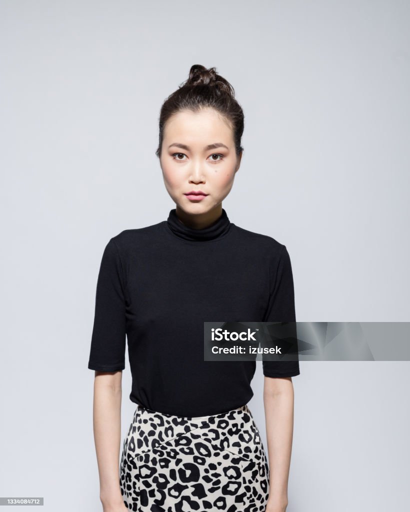 Confident asian young woman Portrait of sad asian young woman wearing black turtleneck and leopard print skirt, looking at camera. Studio shot, grey background. 20-24 Years Stock Photo