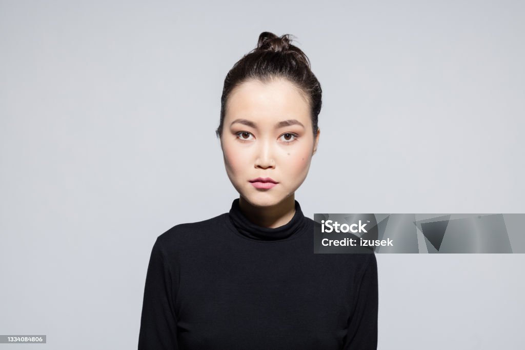 Confident asian young woman Portrait of asian young woman wearing black turtleneck looking at camera. Studio shot, grey background. Asian and Indian Ethnicities Stock Photo