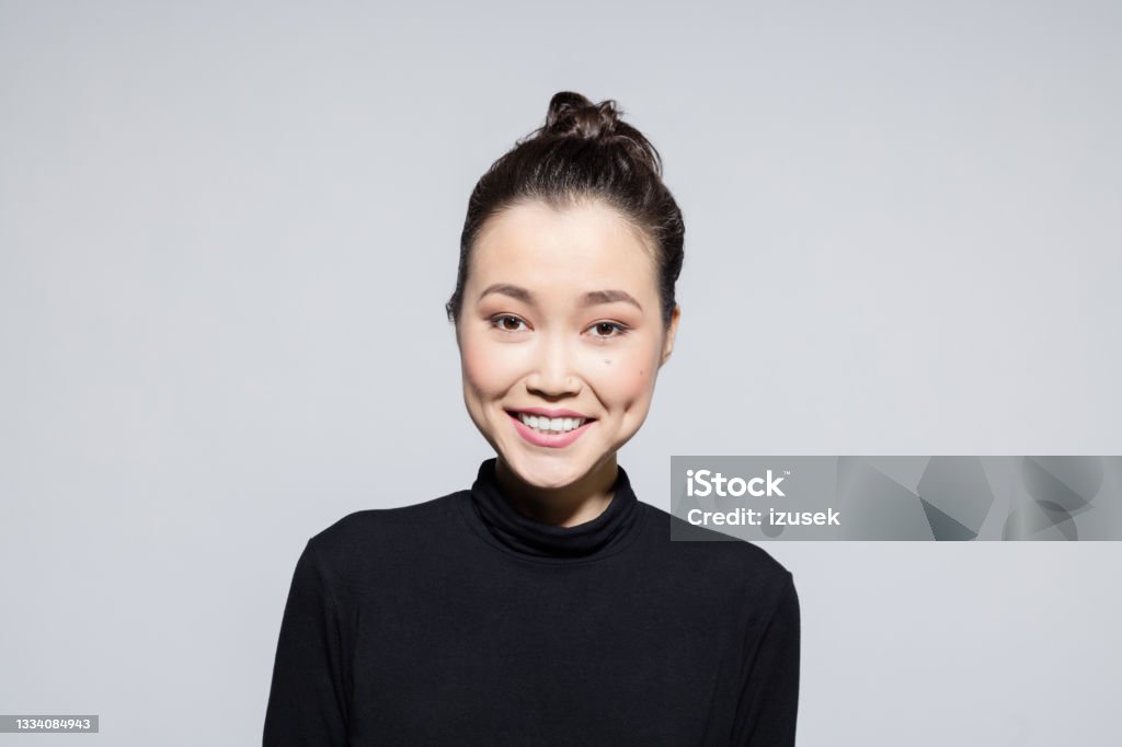 Excited asian young woman Headshot of beautiful asian young woman wearing black turtleneck, smiling at camera. Studio shot, grey background. One Woman Only Stock Photo