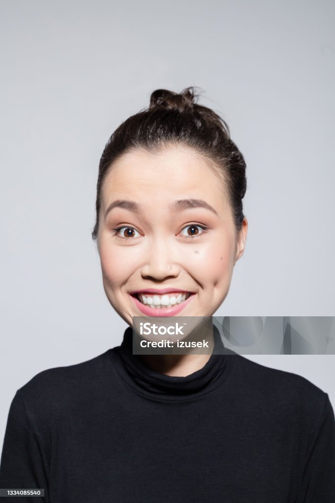 Excited asian young woman Headshot of surprised asian young woman wearing black turtleneck, laughing at camera. Studio shot, grey background. Turtleneck Stock Photo