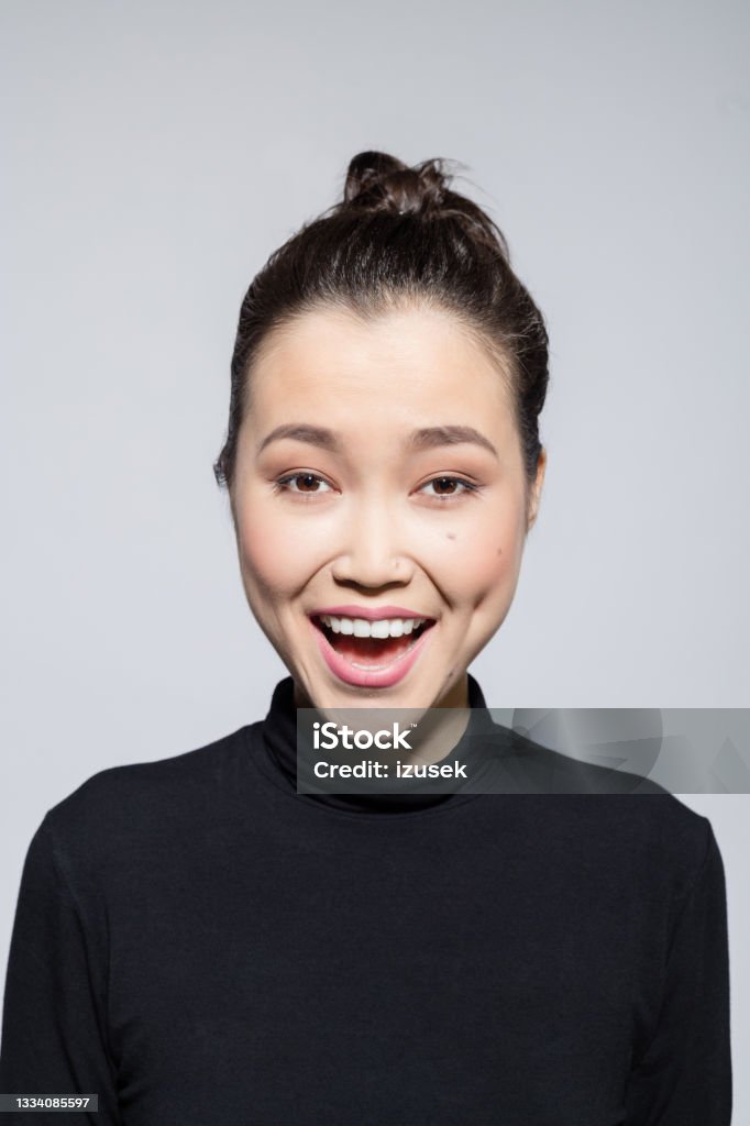 Excited asian young woman Headshot of surprised asian young woman wearing black turtleneck, laughing at camera. Studio shot, grey background. 20-24 Years Stock Photo