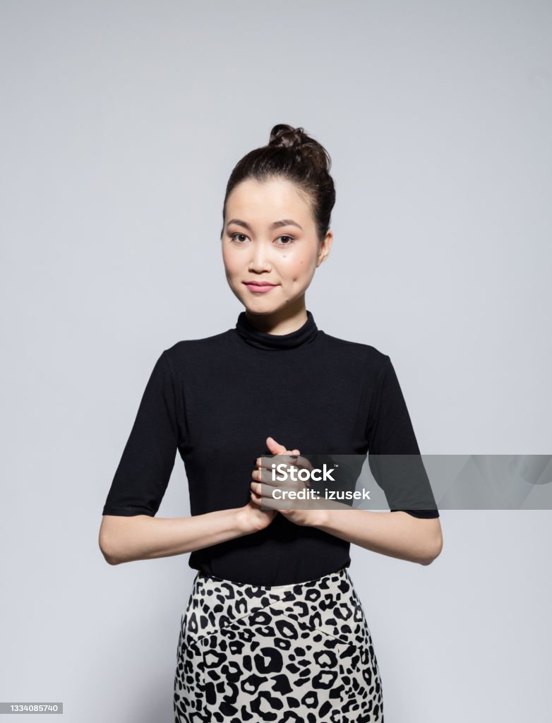 Friendly asian young woman Portrait of beautiful asian young woman wearing black turtleneck and leopard print skirt, smiling at camera. Studio shot, grey background. 20-24 Years Stock Photo