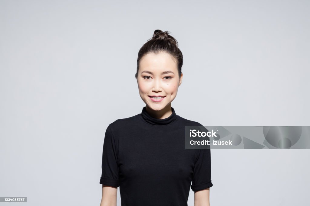 Friendly asian young woman Portrait of beautiful asian young woman wearing black turtleneck, smiling at camera. Studio shot, grey background. 20-24 Years Stock Photo