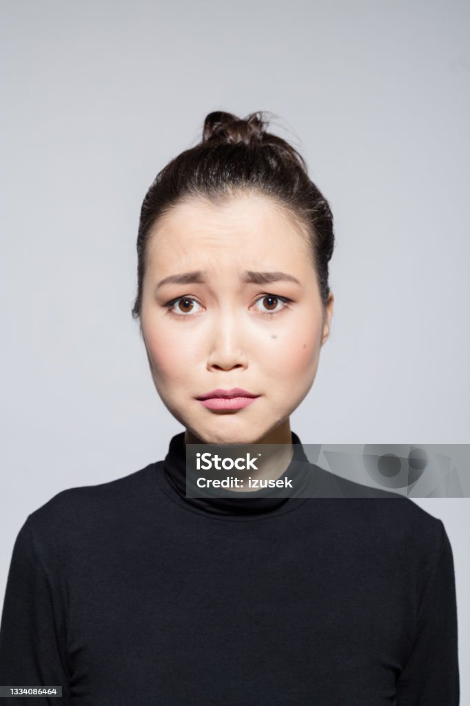 Sad asian young woman Portrait of disappointed asian young woman wearing black turtleneck, looking at camera. Studio shot, grey background. Women Stock Photo