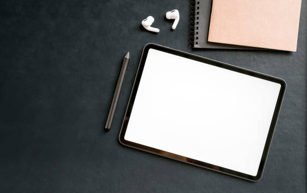 istock Top view blank screen tablet and supplies on black leather background with copy space. 1334086989