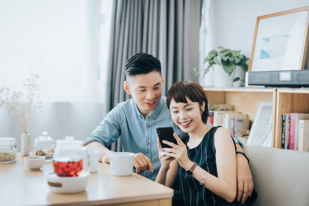 istock Loving young Asian couple using smartphone together while enjoying coffee and relaxing in living room at home 1334088001