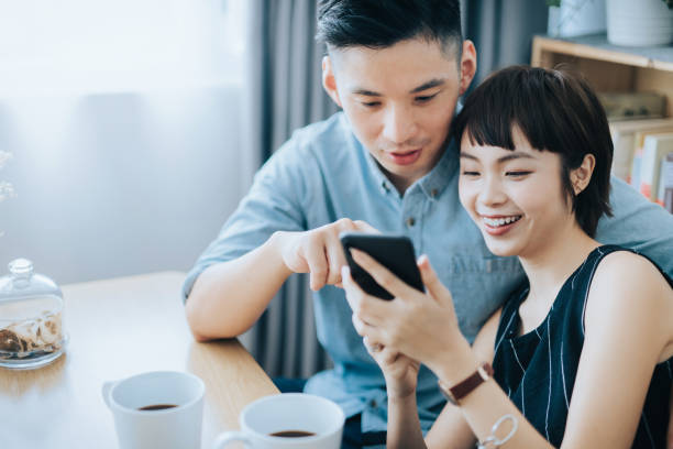 istock Loving young Asian couple making a plan on smartphone together while enjoying coffee and relaxing in living room at home 1334088032