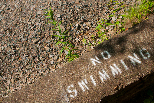 Close up photo of a painted sign along the side of a dried river bank that reads 