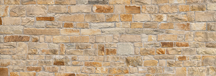 Old panoramic wall made of different sized, square natural stones in beige and brown