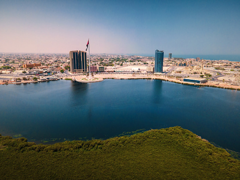 Ras al Khaimah corniche and downtown area of the emirate aerial cityscape landmark skyline rising over the mangroves and the creek water surrounded by seaside and coastline in the United Arab Emirates aerial view.\nUAE northern emirate