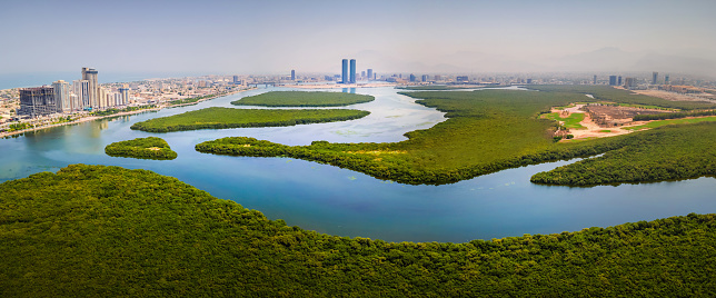 Ras al Khaimah emirate aerial cityscape landmark skyline rising over the mangroves and the creek water surrounded by seaside and coastline in the United Arab Emirates aerial panoramic view.\nUAE northern emirate