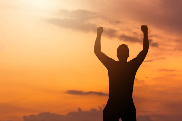 istock Silhouette of a man with hands raised in the sunset. 1334098835
