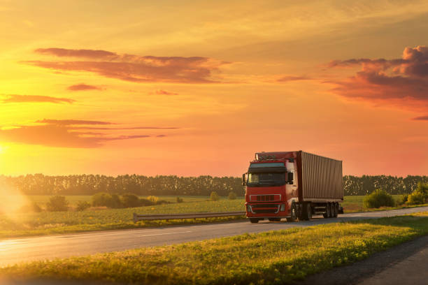 scenic front view big long heavy semi-treailer truck with sea shipping container driving highway dramatic warm morning evening sunrise sky sunset. cargo transport industry background concept. - convoy imagens e fotografias de stock