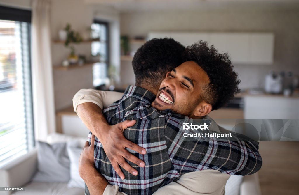 Young happy adult brothers in kitchen indoors at home, hugging. A young happy adult brothers in kitchen indoors at home, hugging. Brother Stock Photo
