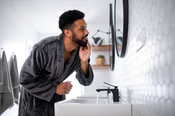 Young man washing face indoors at home, morning or evening routine concept.