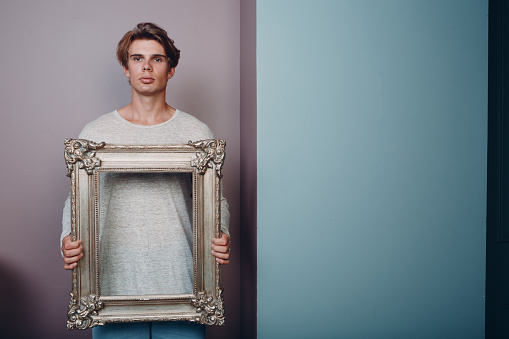 Millenial young man artist with blonde hair on gilded picture frame portrait.