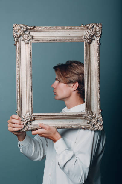 istock Portrait young man standing with picture frame at studio. 1334103955