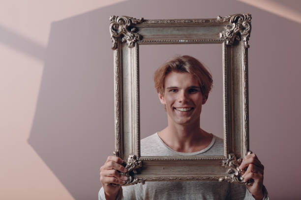 istock Portrait young man standing with picture frame at studio. 1334103965