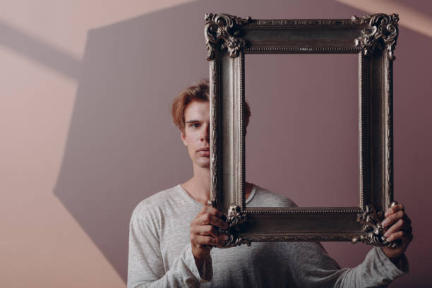 istock Portrait young man standing with picture frame at studio. 1334103969