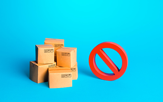 Carton boxes of goods and a red prohibition sign NO. Protection of national manufacturers. Bureaucratic and economic constraints on import-export operations of goods. Free trade market. Protectionism