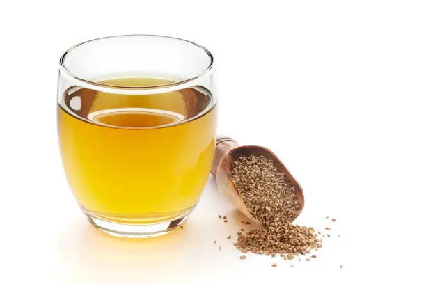 Close-Up of original  organic boiled water (Tea or kada ) with Ajwain ( Trachyspermum ammi ) in a transparent glass cup over white background. Original residue in bottom of tea cup