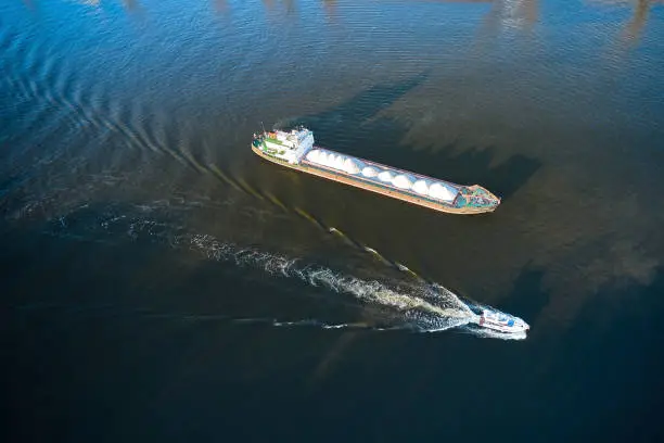 Aerial of the loaded by stacks of sand tanker on a water and motorboat is moving through