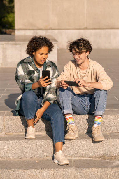 istock Two intercultural teens with smartphones sitting on staircase 1334116051