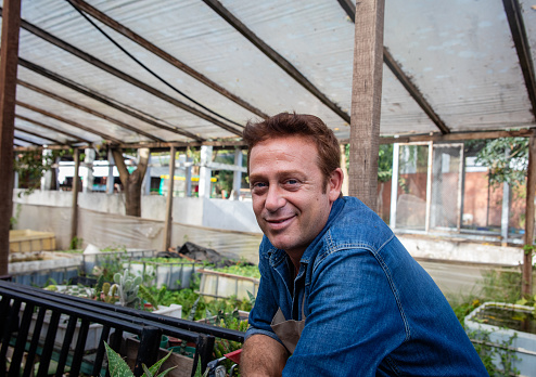 Handsome male owner of a greenhouse taking a break while smiling cheerfully at camera - sustainable lifestyles