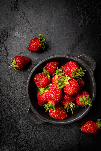 Fresh ripe strawberry in a bowl on dark background, top view, copy space
