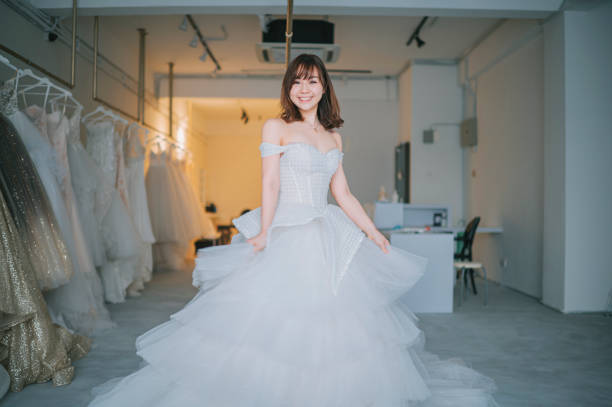 heureux fier satisfait portrait de mariée chinoise asiatique posant en regardant l’appareil photo souriant à la boutique de mariage en essayant de robe de mariée grandi - twisting arm photos et images de collection