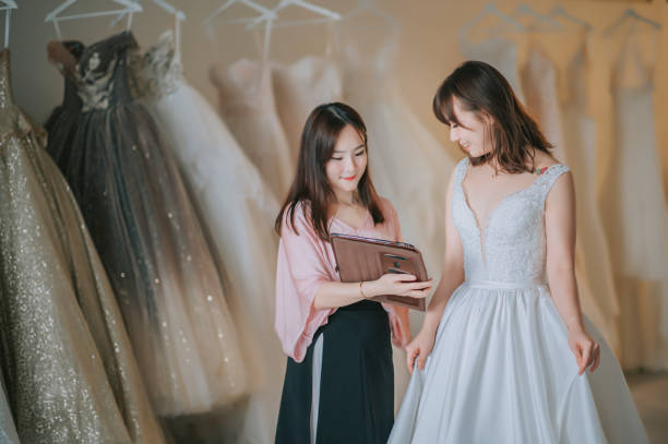 istock Asian chinese female bridal shop owner showing explaining to her customer bride using digital tablet choices package pricing custom made  design wedding dress 1334128809