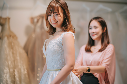 asian chinese wedding dress designer fitting bridal gown to bride to be in boutique. Women checking and making adjustment to wedding gown in professional fashion designer studio.