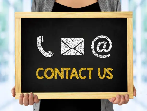Contact us concept, business woman hand holding a chalkboard on office background