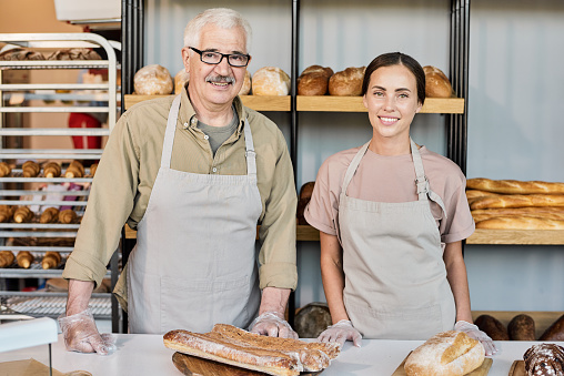 Successful bakers in workwear standing by workplace against display with bread assortment