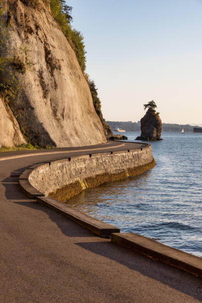 View of the Siwash Rock from Seawall at Stanley Park in a modern city. Downtown Vancouver, British Columbia, Canada. Sunny Summer Sunset.
