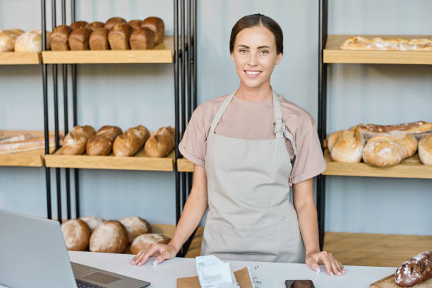 istock Young smiling female clerk standing by counter against display 1334132706