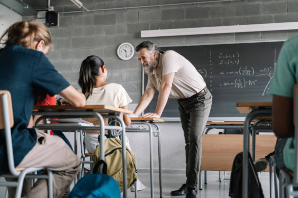 istock Nice teacher with beard helping student in maths science class. Professor talking to girl in the secondary high school classroom 1334135372