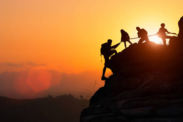 silhouette della squadra di arrampicata che si aiuta a vicenda mentre si arrampica in un tramonto. il concetto di aiuto. - superare le avversità foto e immagini stock