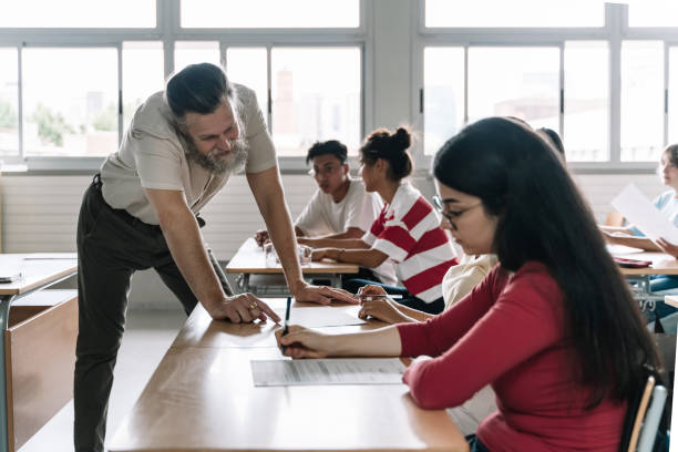istock Friendly Professor explaining exercise to students in secondary school classroom. Senior Teacher with beard helping teenager learning student 1334136262