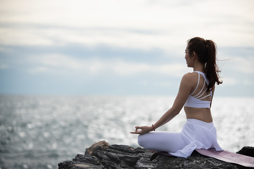 Asian young woman practicing yoga in sukhasana exercise while looking out to the sea.