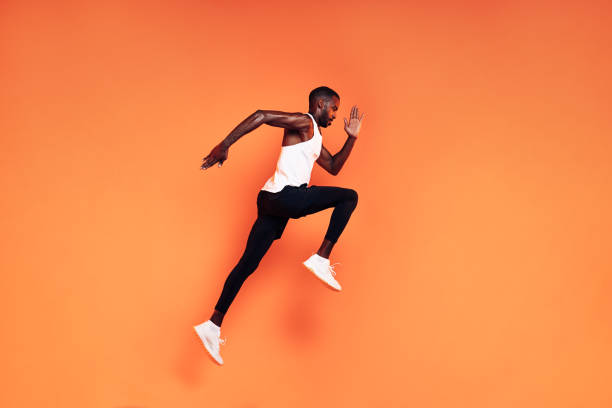 Male runner doing fitness workout. Athlete exercising over an orange background. Male runner doing fitness workout. Athlete exercising over an orange background. sports clothing stock pictures, royalty-free photos & images