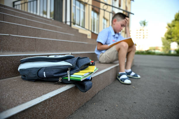 istock Upset worried boy with backpack doing his homework. School bag with copy books and school supplies lying on the stairs. Back to school concept 1334140347