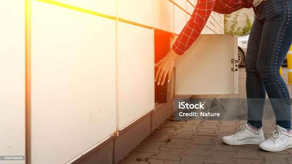Post terminal. Parcel courier box in woman hands at delivery automat terminal. Online selling, e commerce, packing concept. Post terminal. Parcel courier box in woman hands at delivery automat terminal. Online selling, e commerce, packing concept Locker Stock Photo