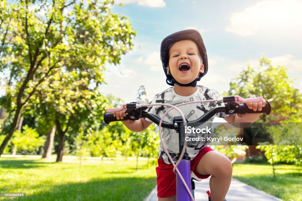 Portrait little cute adorable caucasian toddler boy in safety helmet enjoy having fun riding exercise bike in city park road yard garden forest. Child first bike. Kid outdoors sport summer activities Portrait little cute adorable caucasian toddler boy in safety helmet enjoy having fun riding exercise bike in city park road yard garden forest. Child first bike. Kid outdoors sport summer activities. Cycling Stock Photo