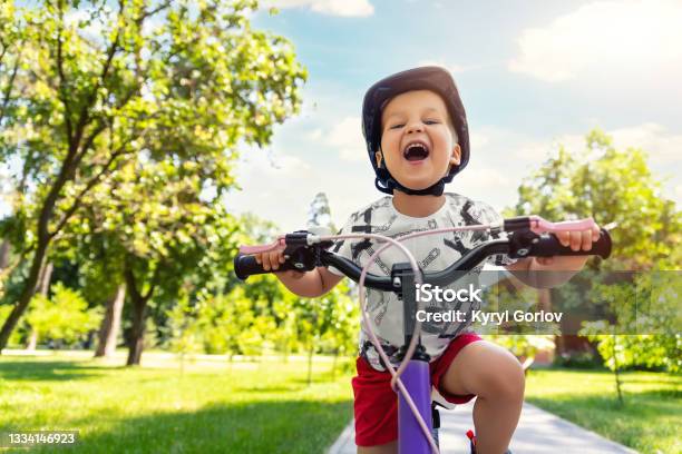 Portrait Little Cute Adorable Caucasian Toddler Boy In Safety Helmet Enjoy Having Fun Riding Exercise Bike In City Park Road Yard Garden Forest Child First Bike Kid Outdoors Sport Summer Activities Stock Photo - Download Image Now