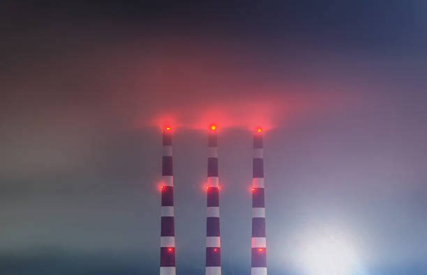 Silhouette of smoking factory pipes against the sunset landscape. Two pipes emit thick smoke.