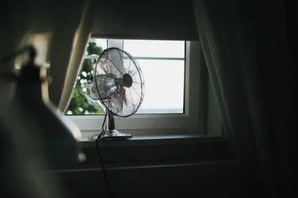 Photo of Cooling fan in the light hot summer night by the open window.