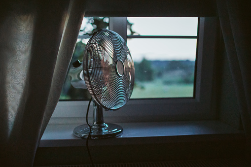 Cooling fan in the light hot summer night by the open window.